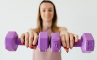 Defocused content young female doing bicep exercise with dumbbells during functional training in light studio
